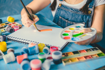 Pretty smiling young woman drawing a picture with poster paint