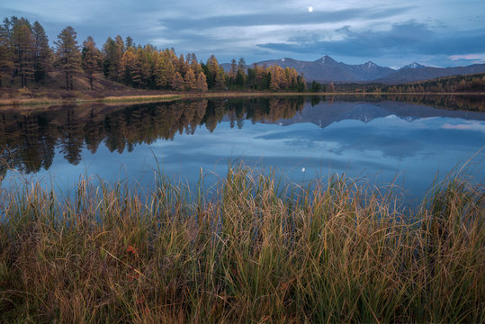 Mirror Surface Lake Autumn Landscape With Mountain Range On Background And Early Evening Moon