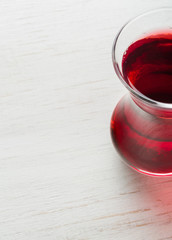 Hibiscus tea in a glass mug on a wooden table among rose petals and dry tea custard