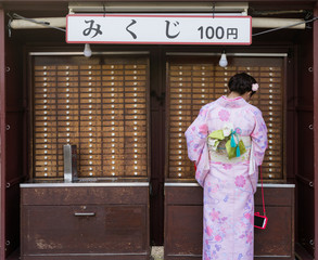 Asian girl in Kimono clothes drawing a fortune slip.