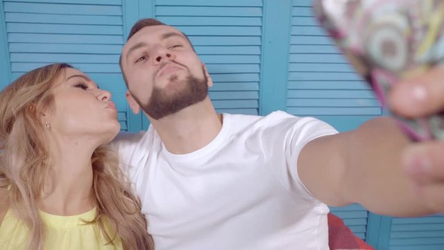 Couple doing a selfie on a mobile phone and build faces on the camera. Man with stylish beard and a girl with white hair.