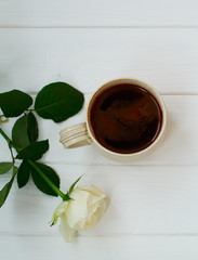 Cup of black coffee and white roses, on white wooden background.