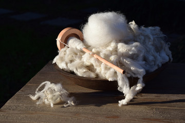 Drop spindle wrapped with handmade yarn in a bowl full of raw wool curls and locks from a sheep.
