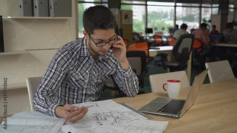 Poster engineer sitting in at the working place on the desk blueprint. young professional man call client t