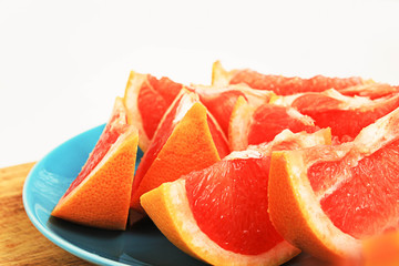 Дольки сочного грейпфрута на голубой тарелке и деревянной кухонной доске.