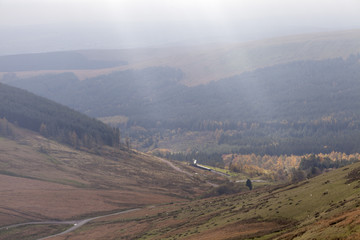 View over Torpantau valley. The view over Torpantau valley in the Brecon Beacons. Sunlight streams through the overcast skyline and in the distance the tourist steam train can be seen.