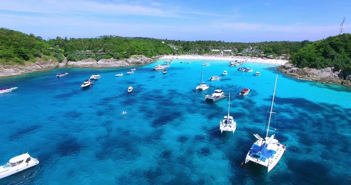 Racha Island Beach. Thailand, Phuket. Yachts , Catamarans and Boats sailing in crrystal clear blue water of ocean. Flying from ocean to sandy beach. Aerial view. 4K.