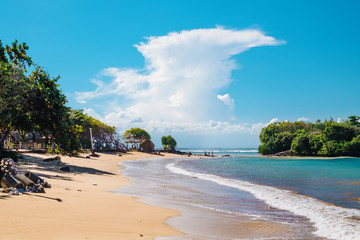 Beautiful outdooor landscape of white sand beach with tropical palm trees in Nusa Dua, Bali island, Indonesia. Blue sky with fantastic white clouds at a sea shore with tropical island exotic nature