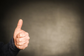 Hand mit Daumen nach oben / Positive Emotion, Hand mit Daumen hoch vor dunklem Hintergrund mit...