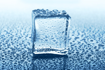 Transparent ice cube with reflection on blue glass with water drops