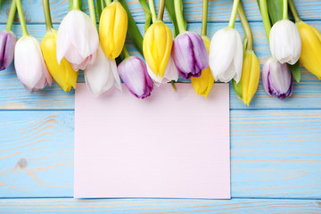 Bouquet of tulips with sheet of blank paper on blue wooden table