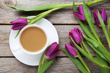 Bouquet of tulips with cup of coffee on grey wooden table