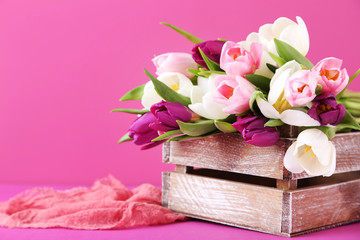 Bouquet of tulips in crate on pink background