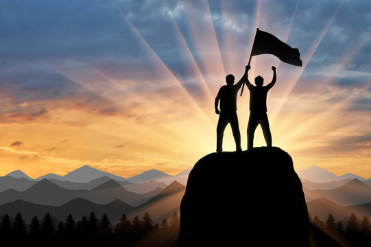 Silhouette of two climbers on a mountain top with a flag in his hand