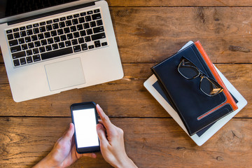 Hand using blank white screen smart phone near notebook, laptop,
