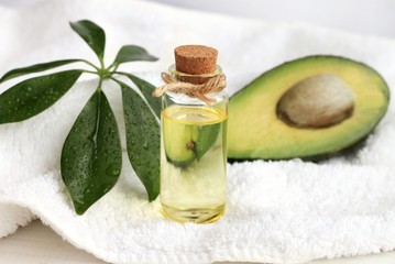Obraz na płótnie Canvas Avocado oil domestic beauty treatment use. Bottle of oil-based tonic, green plant decor on towel and fresh fruit.