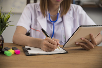 Doctor woman writing to report a patient at the hospital,she is using the tablet.