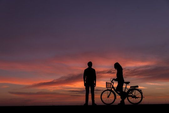 Silhouette of lovers standing  with vintage bikes on the side.The background image is a sunset in Thailand.