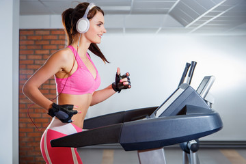 Young smiling girl with headphones running on a treadmill in a sport club. The concept of sport and active lifestyles.