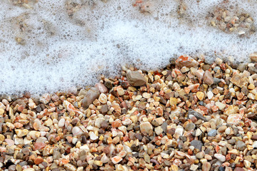 Summer background: Sea water foam and pebbles on the beach
