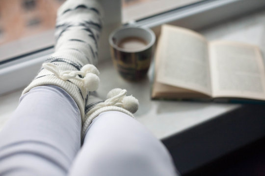Female legs with hot drink and book