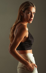 Suntanned girl in bra-top, pants on gray background.