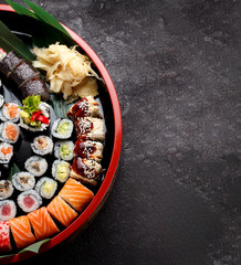 Japanese cuisine. Sushi set on a round wooden plate and dark concrete background.