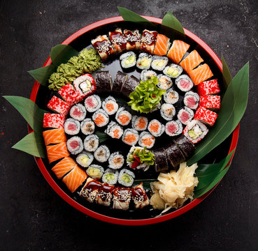 Japanese cuisine. Sushi set on a round wooden plate and dark concrete background.