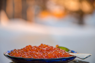 blue plate with metal spoon. red caviar in the snow.