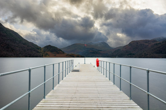 Long pier with British flag pole at Ullswater in the Lake District with moody dramatic clouds.