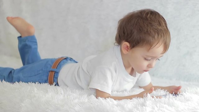 Child boy lying on his stomach looking at an electronic smartphone display