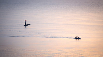 silhouette sunrise of fishery boat sail on calm sea with lightho