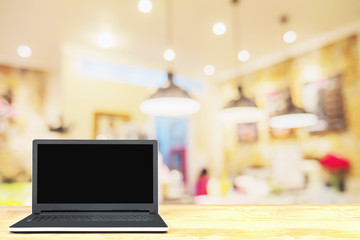Laptop on wooden table over blurred photo of beautiful coffee shop for background use