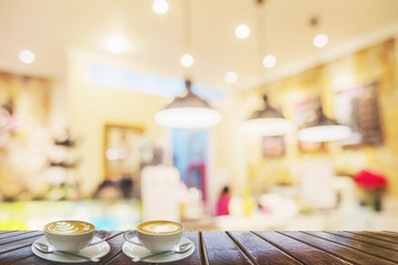 Two coffee cups on brown wooden table over blurred photo of beautiful coffee shop for background use
