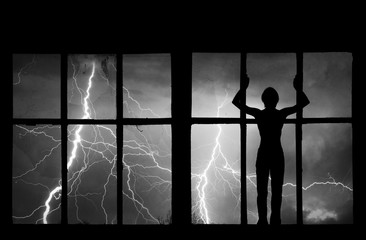 Fototapeta premium Silhouette of man watching lightning, thunder, rain and storm through the broken window of abandoned building