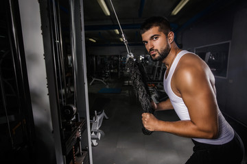 Fototapeta na wymiar Muscular young man is doing exercise on pulldown machine in the gym