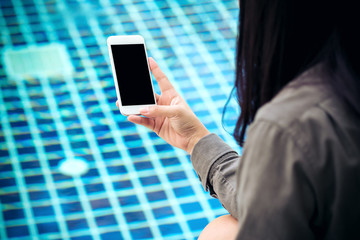 Mockup image of a woman holding and showing smart phone with blank black screen by swimming pool