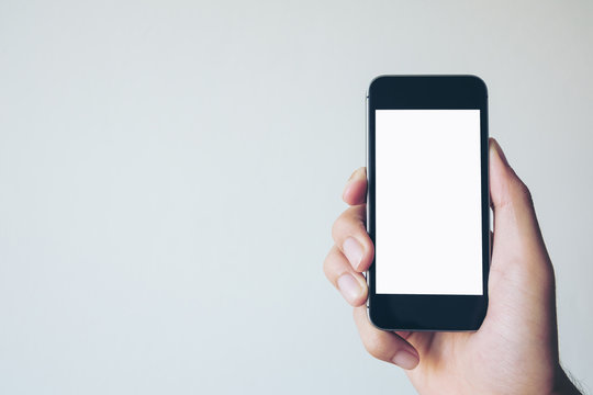 Mockup image of a hand holding black mobile phone with blank white screen on white background room