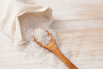 Fototapeta na wymiar sea salt in the bag and wooden spoon on white wooden background