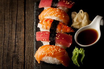 Sashimi and sushi rolls on a stone slatter. Sushi set with salmon, prawns, soy souce, wasabi and ginger. Traditional Japanese cuisine.
