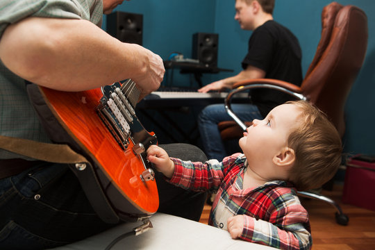 Music rock Band Rehearsal Friendship Together. the baby on a father's musical repetion. The man plays the electro guitar, and his friend on a synthesizer.
