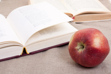 Composition with red apple and opened books on the table, on the