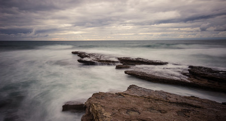 Rocky beach seascape at sunrise. Long exposure from the rocky shore in the Portuguese coast, near Ericeira in Portugal
