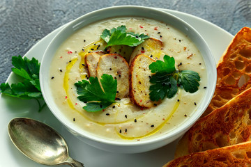 Creamy chicken soup with vegetables in bowl with chiabatta toast, parsley and nigela seeds sprinkle on stone table