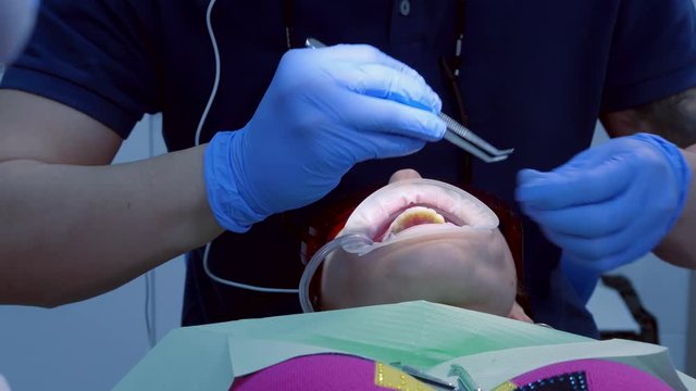 Visit to the dentist. Man doctor makes the procedure painless to the patient girls. The girl in the chair is with the expander in his mouth.