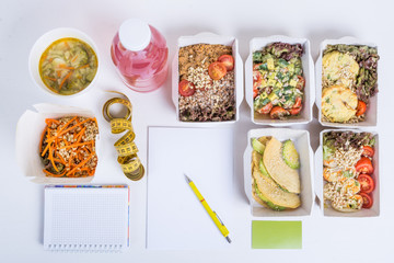 План здорового питания на день для одного человека. Блюда в крафт коробках, блокнот, ручка, визитка, сантиметровая лента и деток-вода на белом фоне.