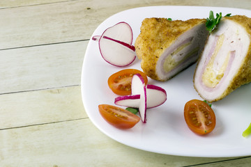 Chicken cordon bleu with vegetables on light wood background