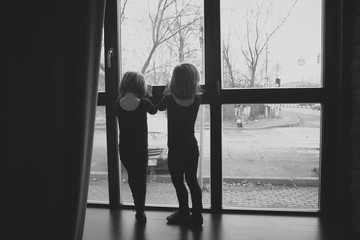 Fototapeta na wymiar Two little girl in a black suit looks out the window black and white photo