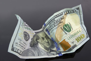 Moderately crumpled 100 dollar bill on gray background.