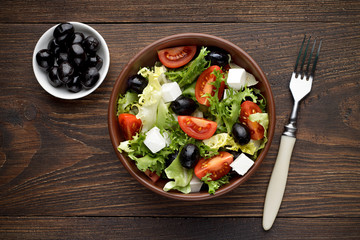 Fresh greek salad in bowl on the wooden table.